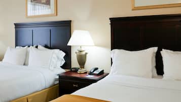 Quarto de hotel com duas camas, mesa de cabeceira com abajur, telefone e relógio.