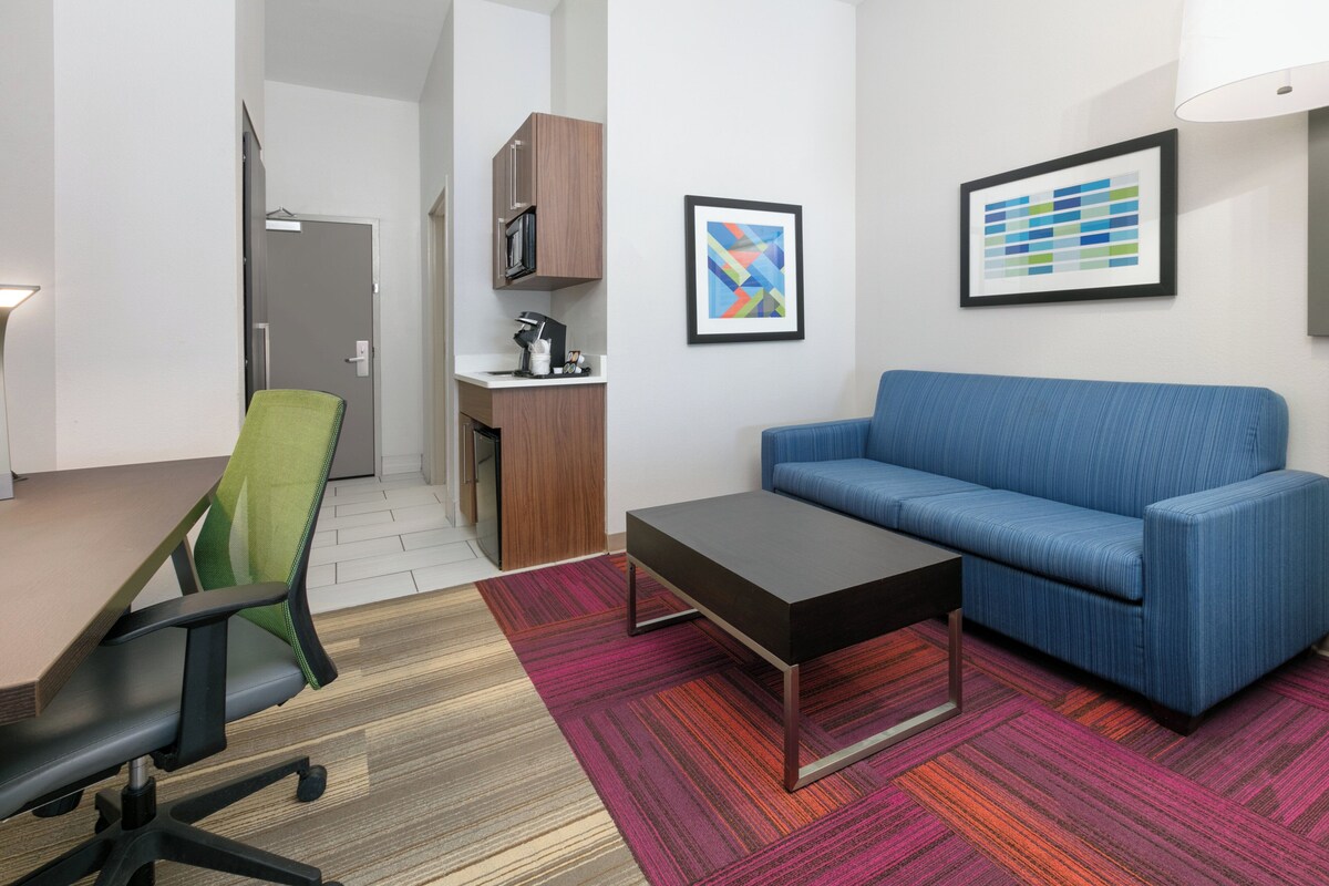 A modern office space with a green office chair, a blue sofa, a coffee table, and a kitchenette.