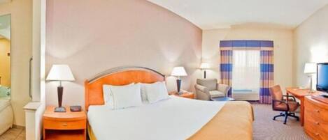 A hotel room with a large bed, two bedside tables with lamps, a desk with a chair, and a television.