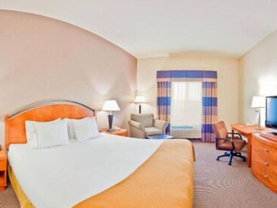 A hotel room with a large bed, two bedside tables with lamps, a desk with a chair, and a television.