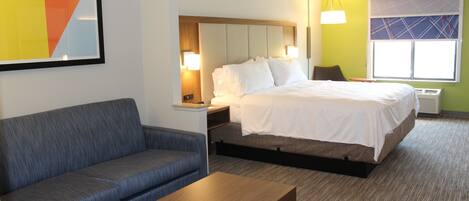 A hotel room with a bed, a sofa, a wooden table, a nightstand, and a wall-mounted lamp.