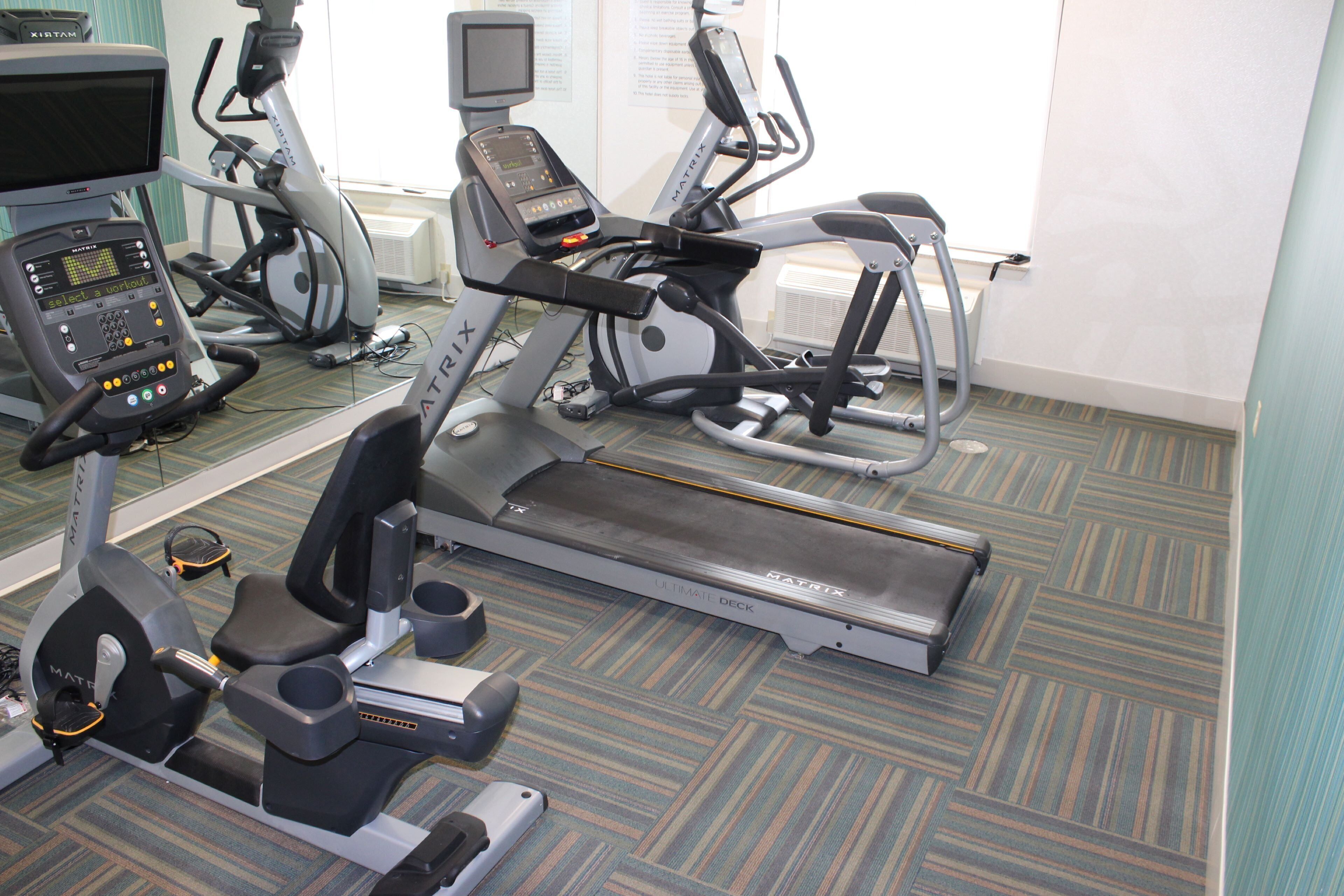 Un gimnasio con equipo de ejercicio variado, incluyendo cintas de correr, una elíptica y una bicicleta estática.