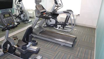Un gimnasio con equipo de ejercicio variado, incluyendo cintas de correr, una elíptica y una bicicleta estática.