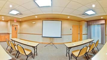 A conference room with a large projection screen, two long tables, and chairs.