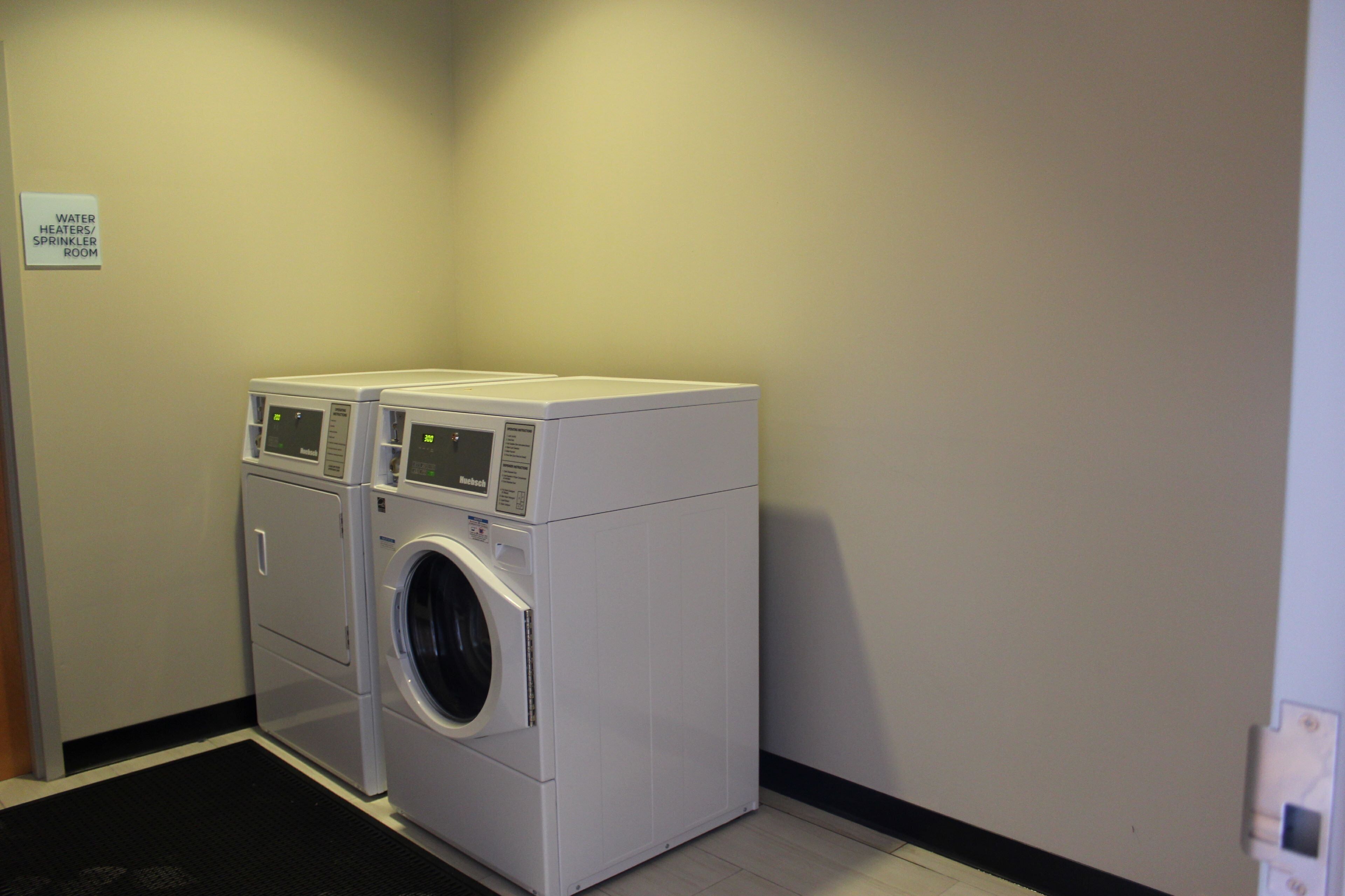 A laundry room with two stacked front-loading washing machines and a sign indicating the location.