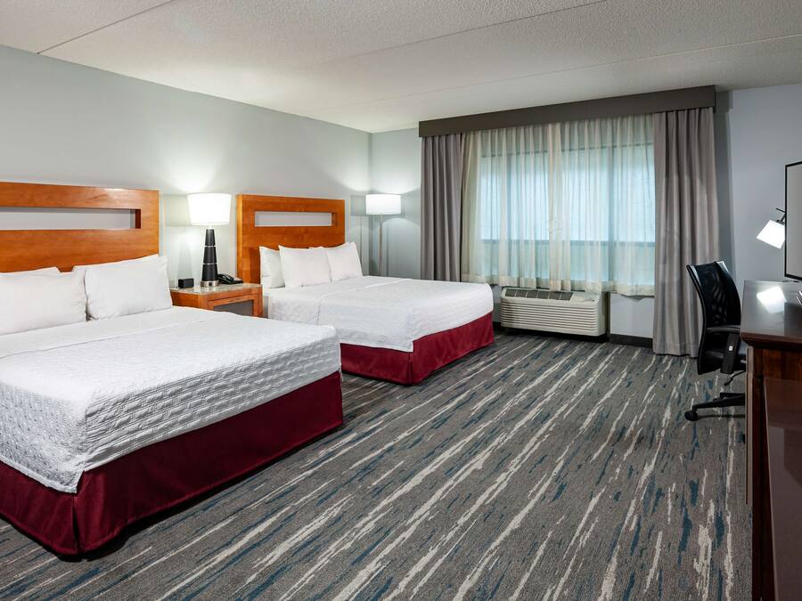 A hotel room with two beds, a television, a desk, and a window with curtains.