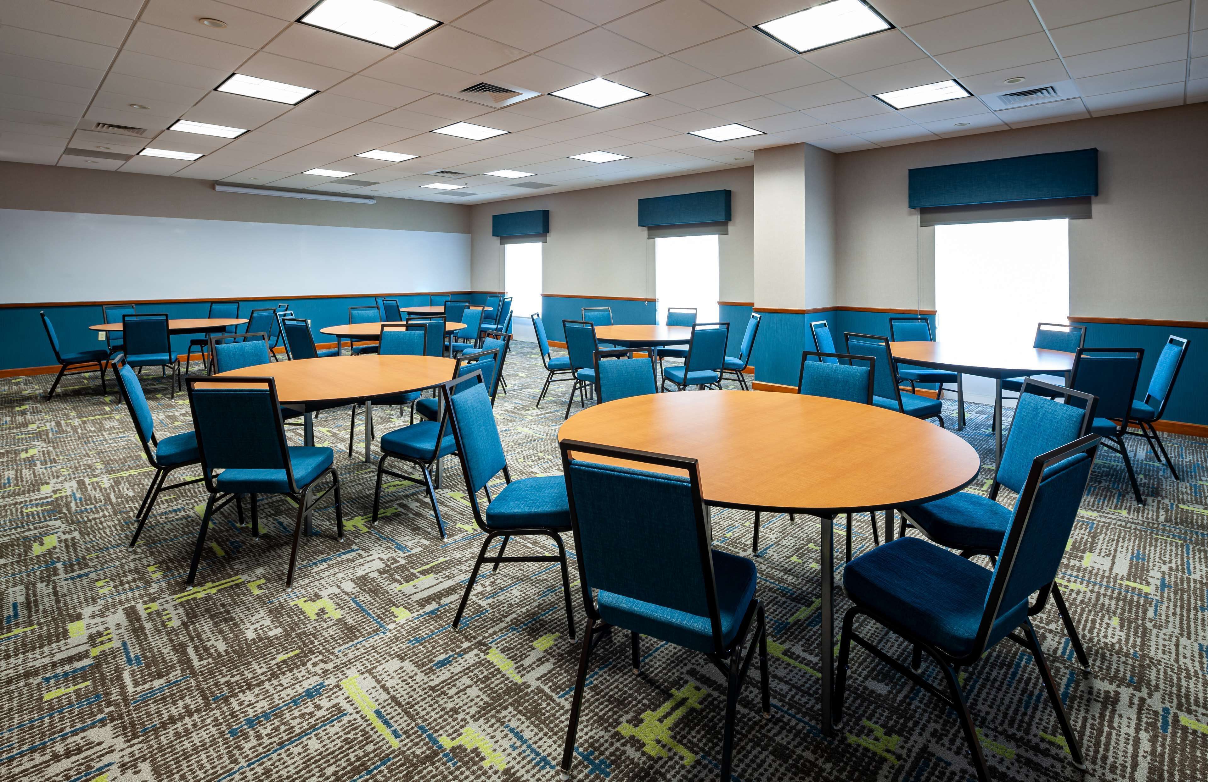 A conference room with multiple tables and chairs, carpeted floor, and large windows.
