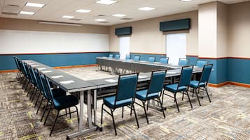A conference room with a long table, blue chairs, and a patterned carpet.