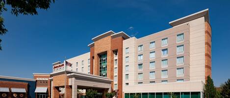 A hotel with a modern design, featuring a large entrance with a covered area, multiple floors, and a parking lot.