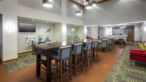 A spacious room with a long table and chairs, a television mounted on the wall, and a 'Welcome to the Show Nest' sign. - Hampton Inn & Suites St. Louis at Forest Park (St. Louis)