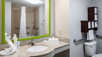 A bathroom with a granite countertop, a white sink, a mirror with a green frame, a shower with a glass door, and a towel rack with white towels.
