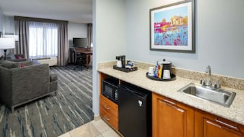 A hotel room with a kitchenette, a sofa, a desk, and a television.