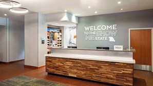 A hotel reception area with a modern design, featuring a reception desk, a wall with a welcome sign, and a view of the lobby. - Hampton Inn & Suites St. Louis at Forest Park (St. Louis)