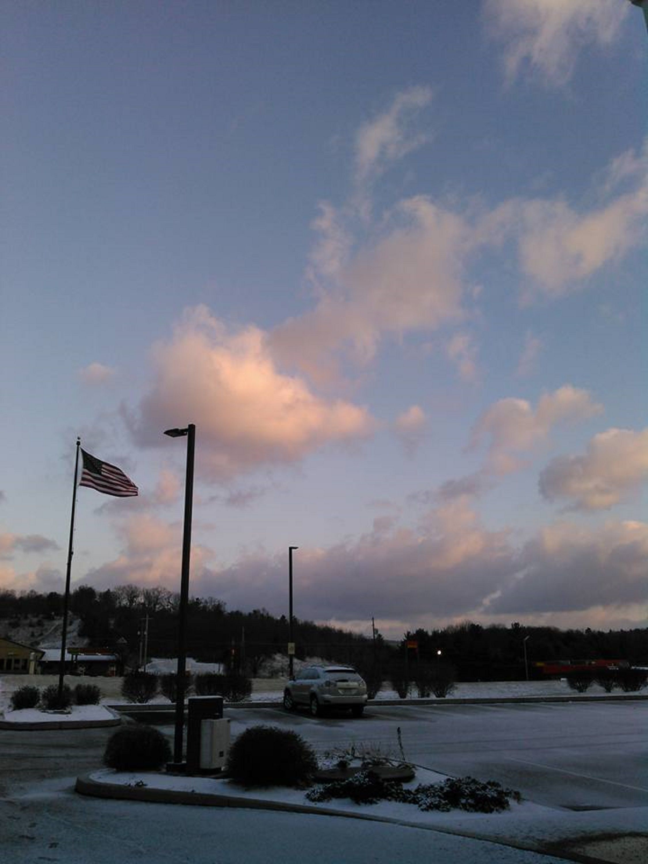 A parking lot with snow on the ground, an American flag, and a building in the background.