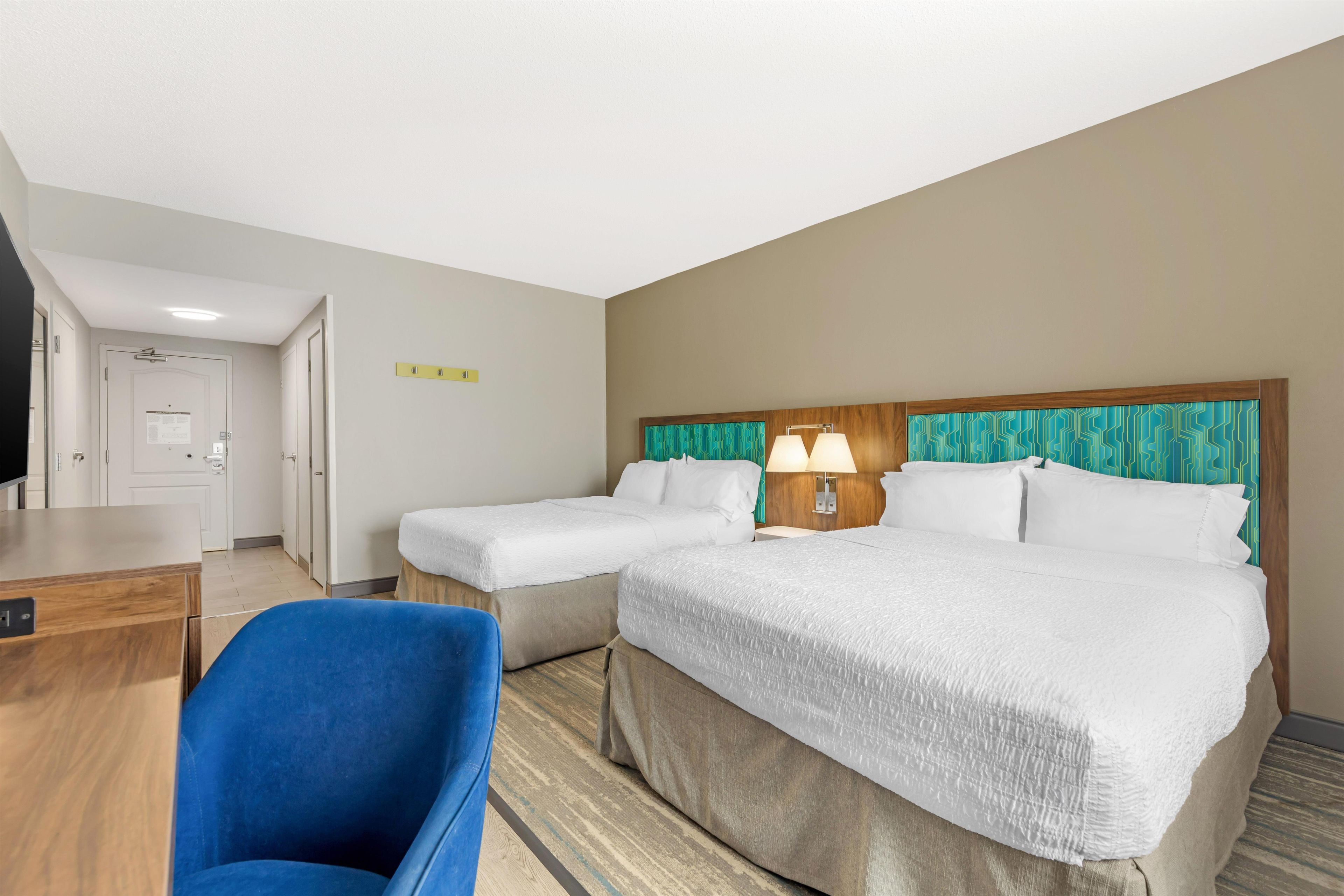 A hotel room with two beds, a desk, and a chair.