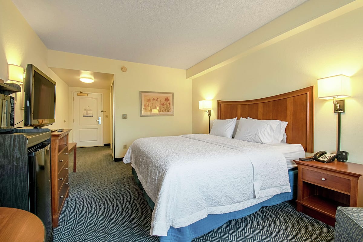 Une chambre d’hôtel avec un lit, une table de chevet, une lampe et un téléviseur posé sur un meuble.