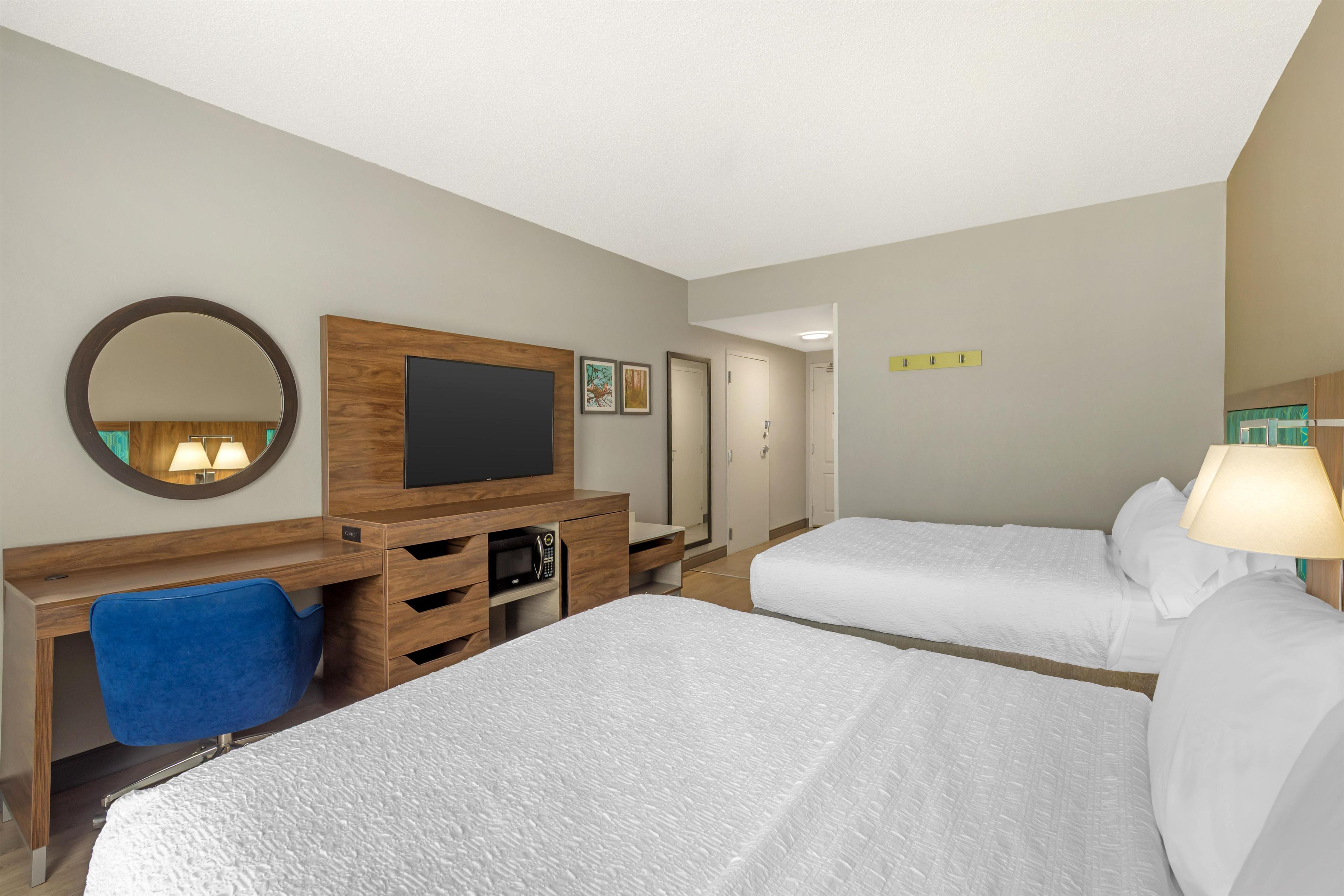 A hotel room with two beds, a desk with a chair, a television, a mirror, and a door.
