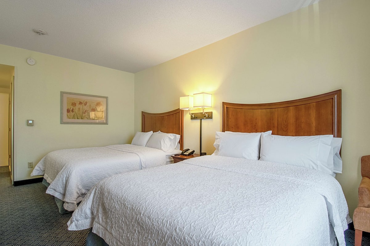 Une chambre d’hôtel avec deux lits, une table de chevet, une lampe et un tableau au mur.
