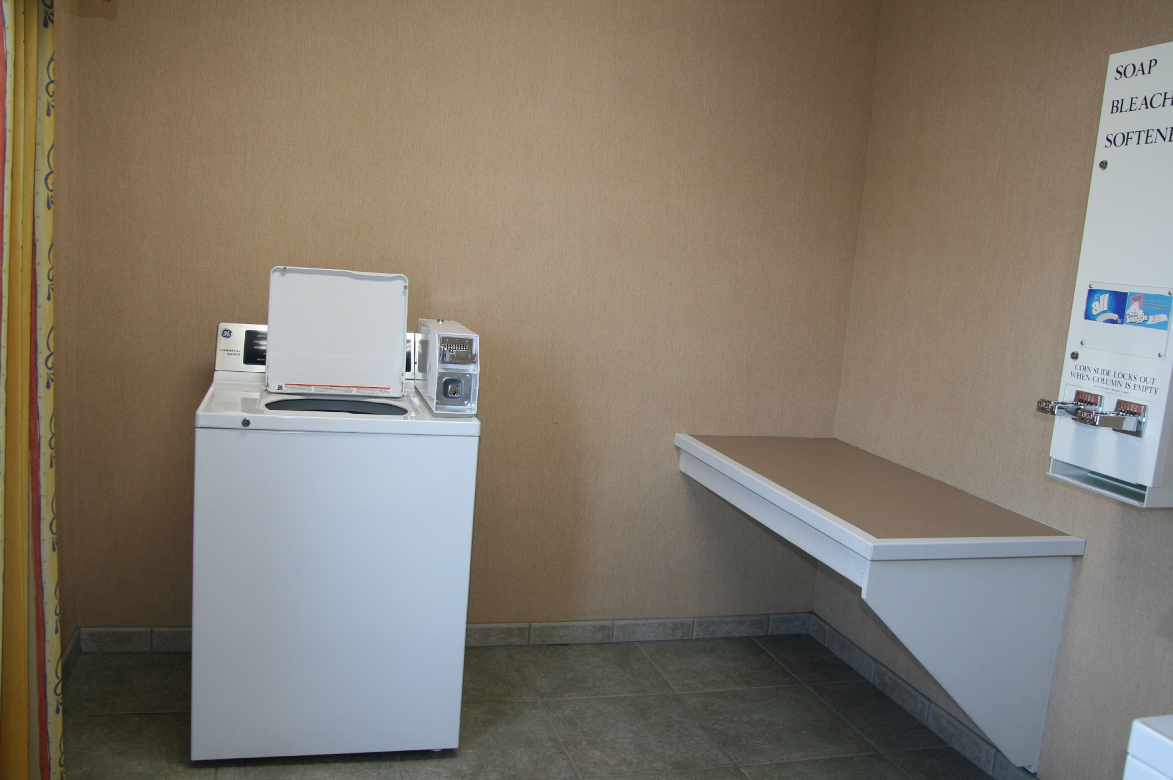 A laundry room with a washing machine and a wall-mounted soap dispenser.