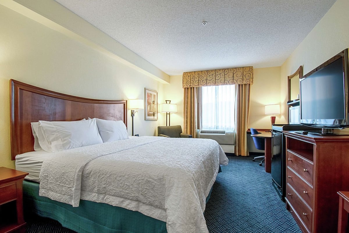 Une chambre d’hôtel avec un grand lit, un bureau, une chaise, une télévision et une commode.
