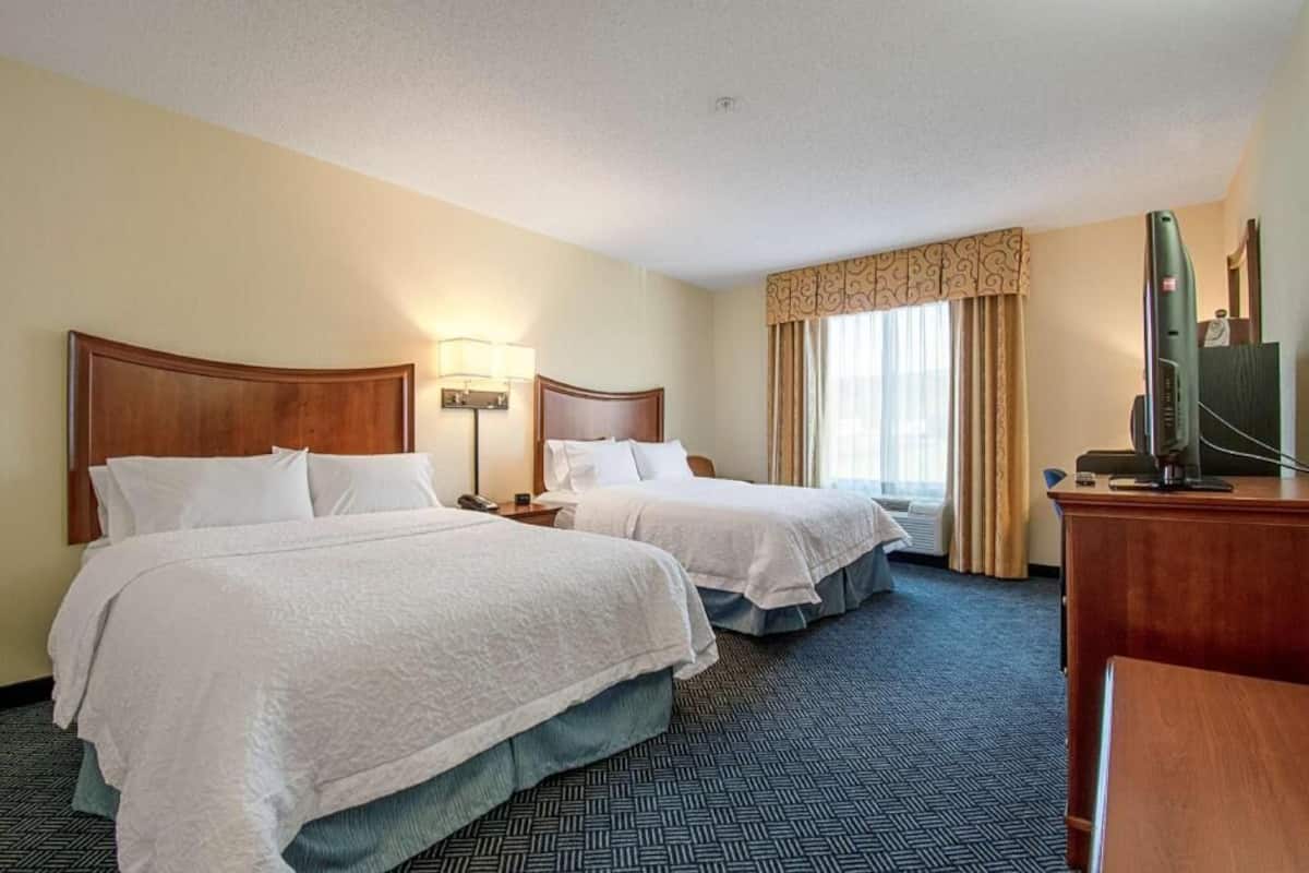 A hotel room with two beds, a desk, a television, and a window with curtains.