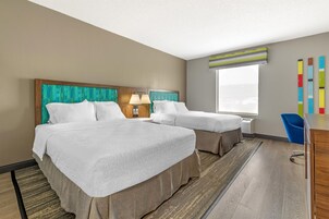Una habitación de hotel con dos camas, un escritorio, una silla y un ventanal grande.