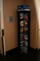 Estante vertical con folletos turísticos y un letrero que recomienda usar las escaleras de emergencia en caso de incendio.