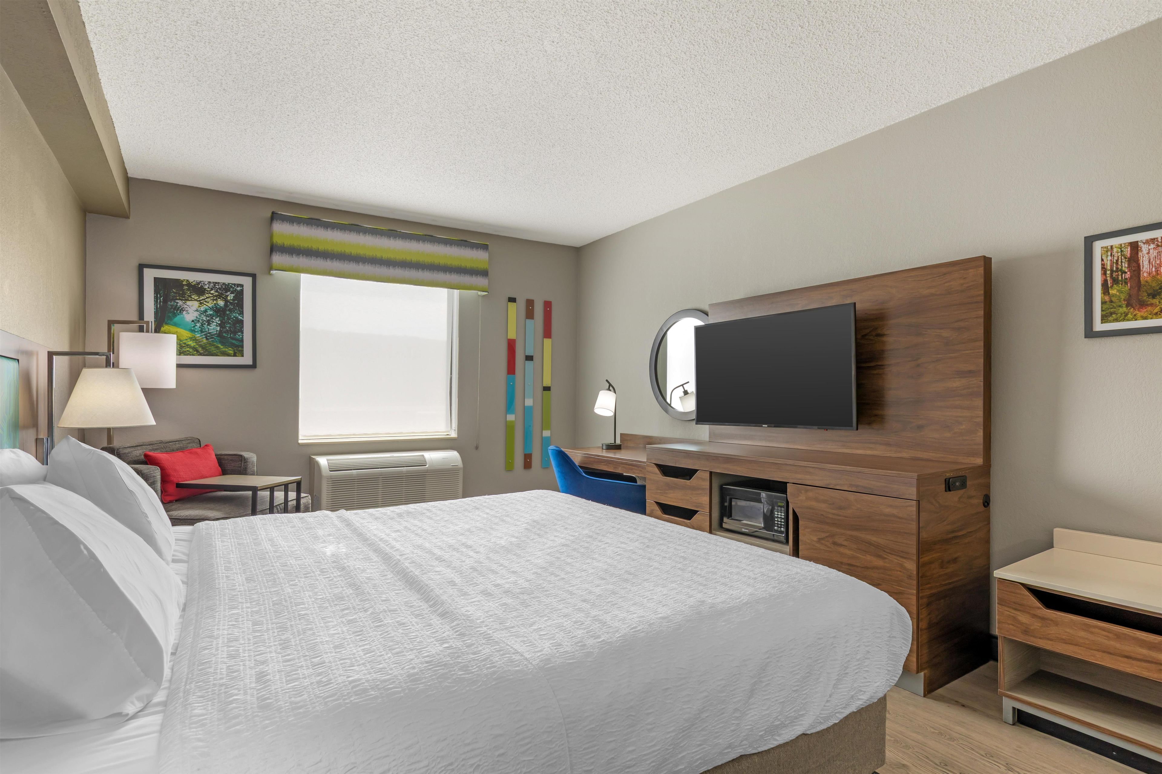Una habitación de hotel con cama, escritorio, televisor y ventana.