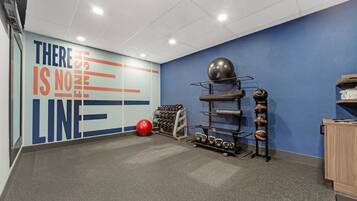 Un gimnasio con equipo de ejercicio, un mural motivacional y una pared azul.