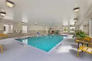 A swimming pool with clear water, surrounded by yellow chairs and a bench, with a lifebuoy and a door in the background. - Hampton Inn Pine Grove (Pine Grove)