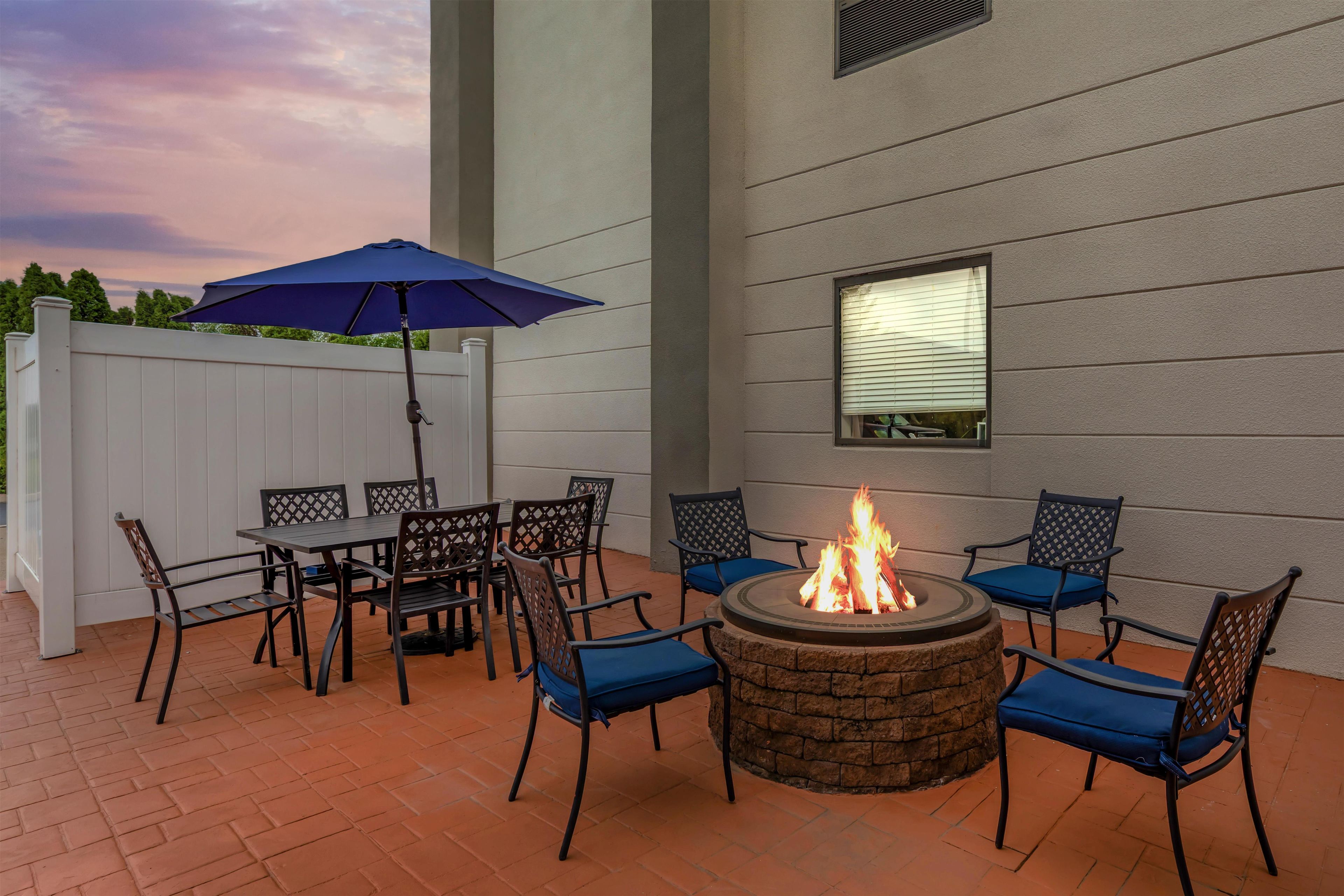 An outdoor patio with a fire pit, seating, and a white fence.