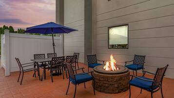 An outdoor patio with a fire pit, seating, and a white fence.