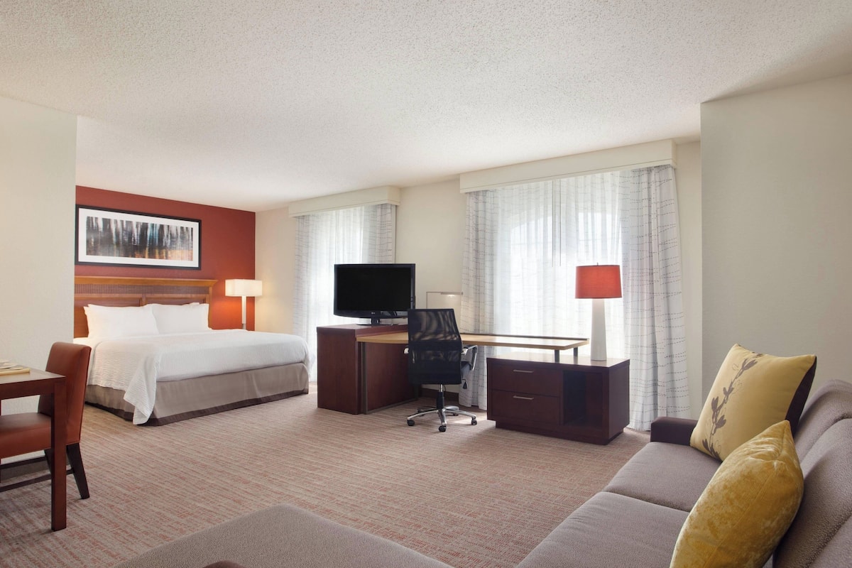 A hotel room with a bed, desk, TV, and seating area.