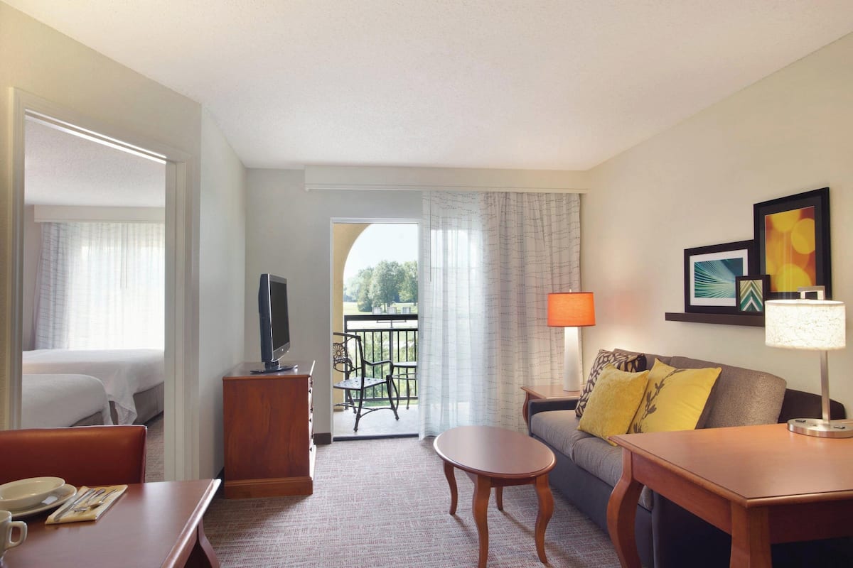 A hotel room with a bed, a TV, a dining table, a sofa, and a balcony with a view.