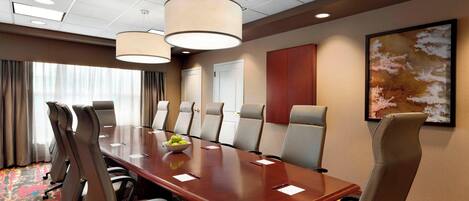 Un salón de conferencias con una larga mesa, varias sillas, un frutero y un cuadro en la pared.