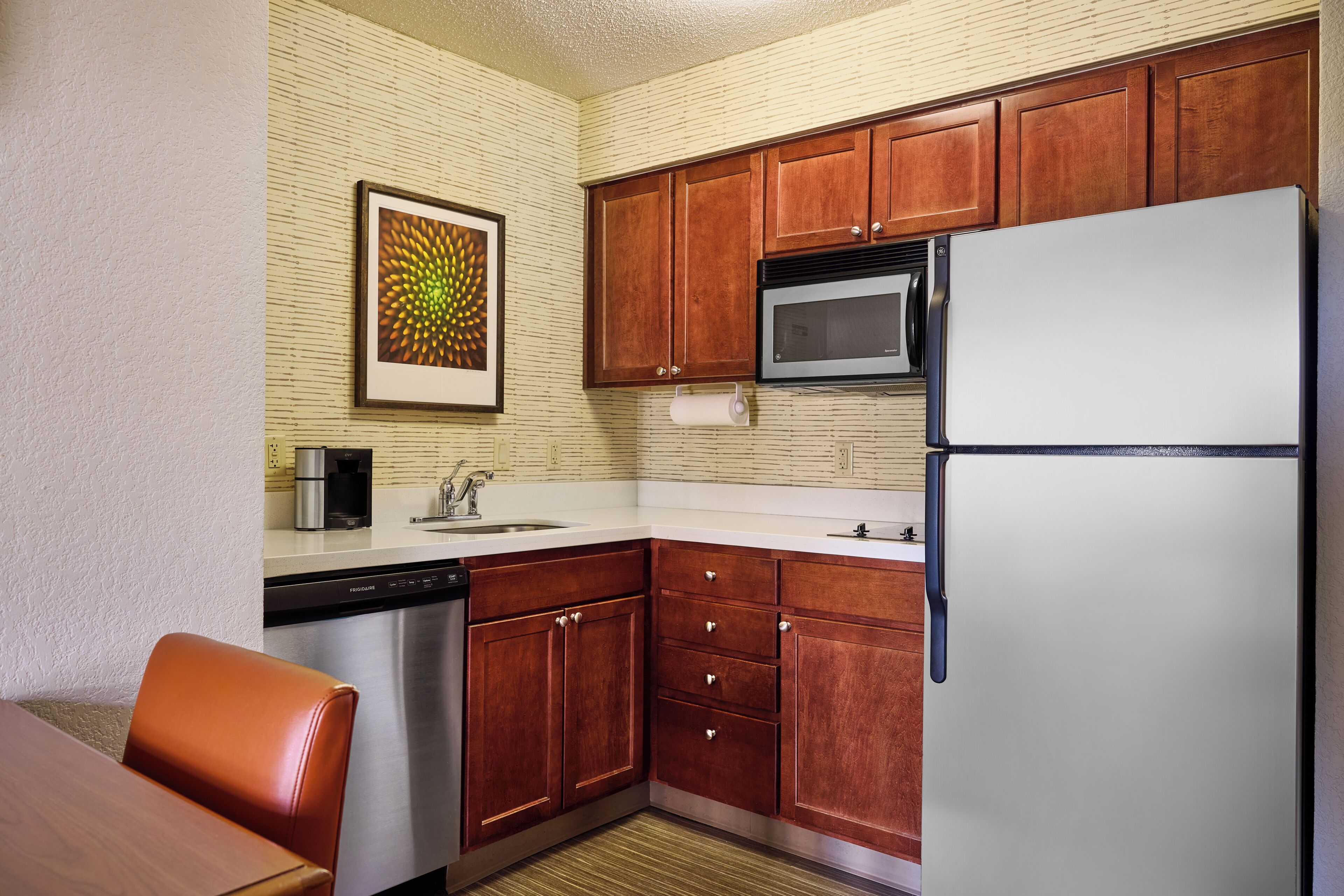 Una cocina compacta con armarios de madera, lavavajillas de acero inoxidable, microondas y refrigerador.