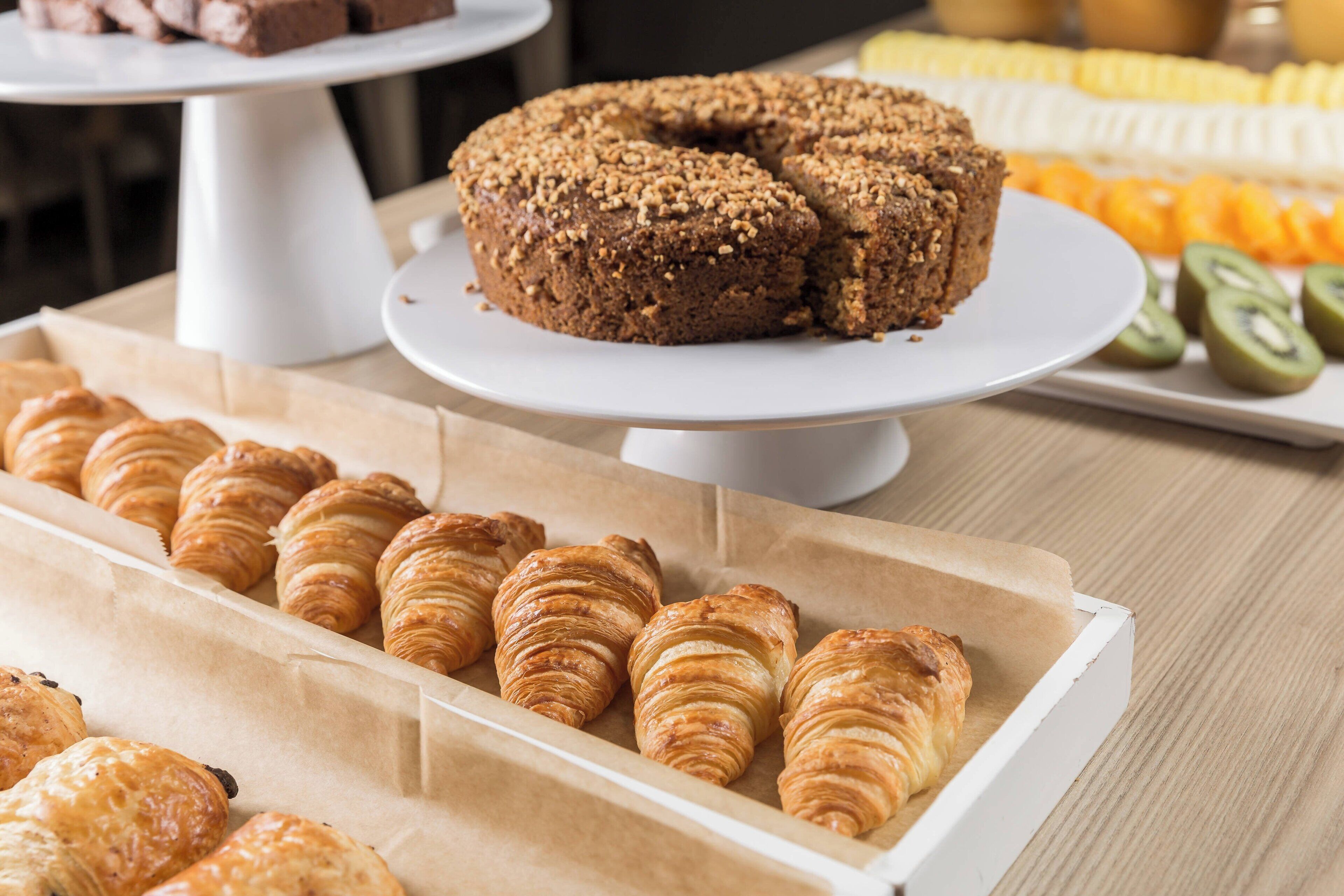A variety of baked goods including a bundt cake, croissants, and pastries on a wooden table.