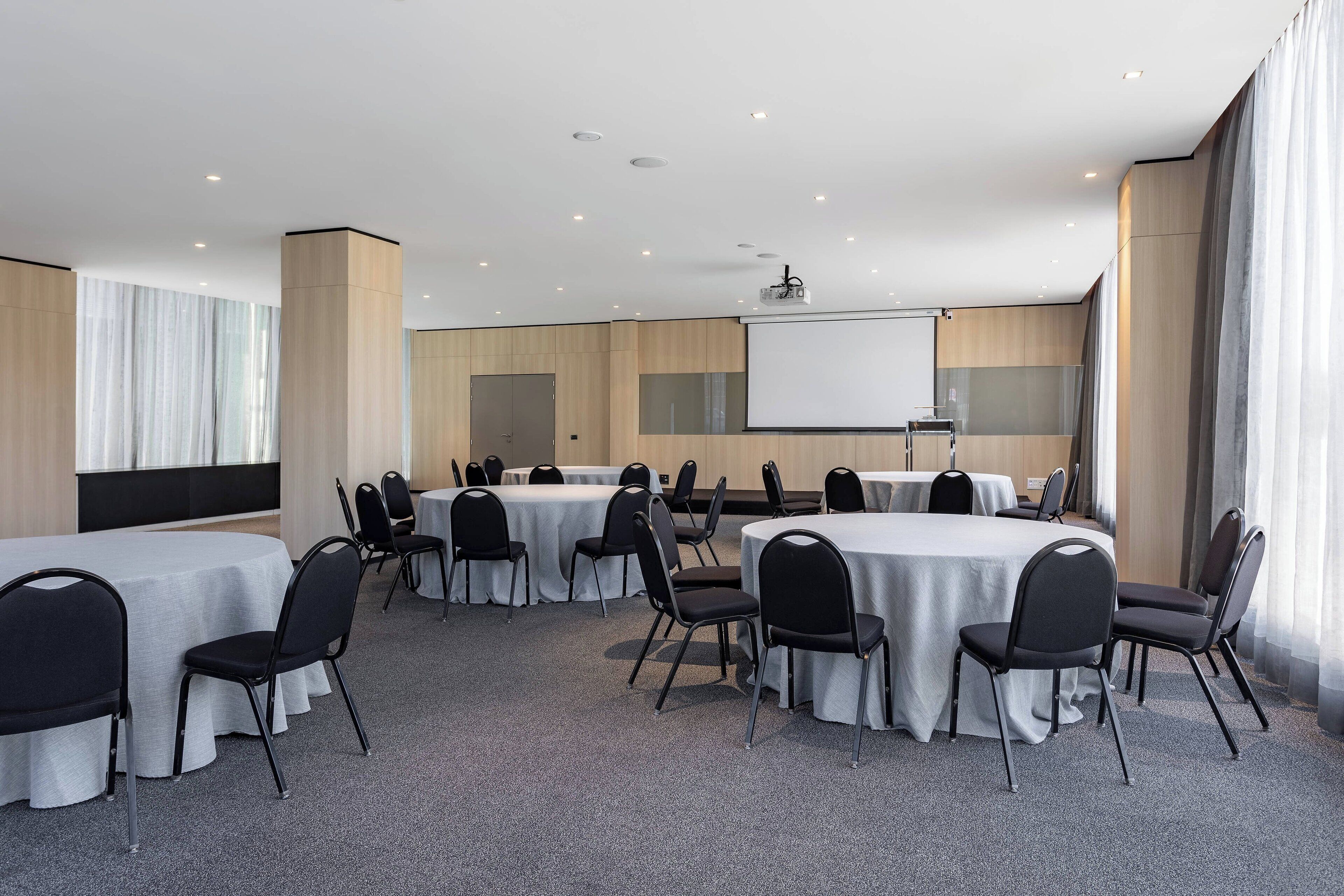 A conference room with round tables, black chairs, a projector screen, and a whiteboard.