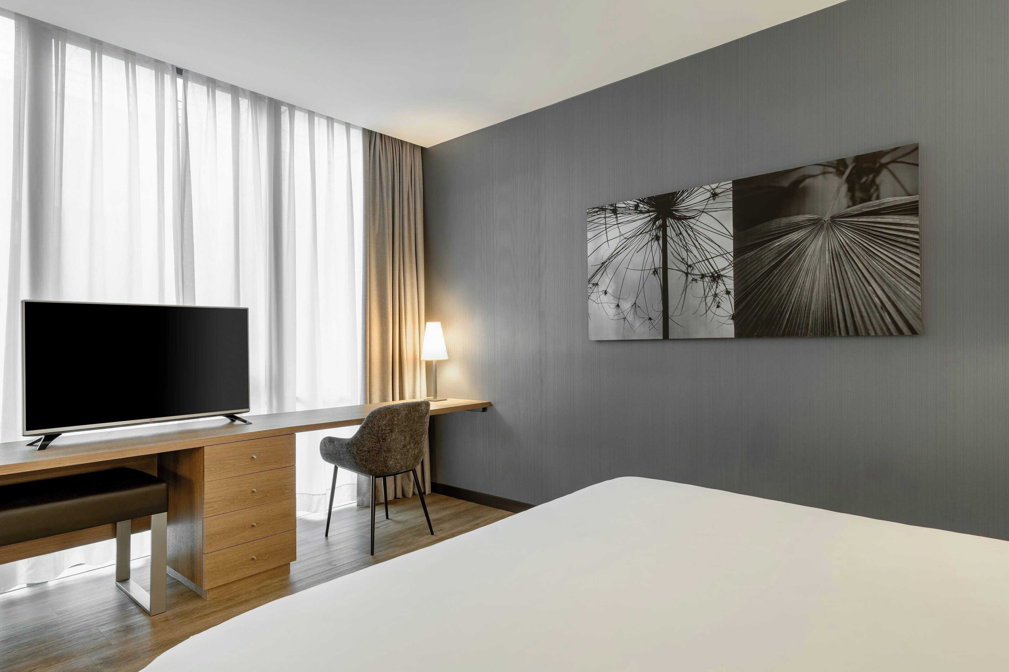 Une chambre d’hôtel avec un grand lit, un bureau doté d’un téléviseur à écran plat, une chaise et deux œuvres d’art murales.