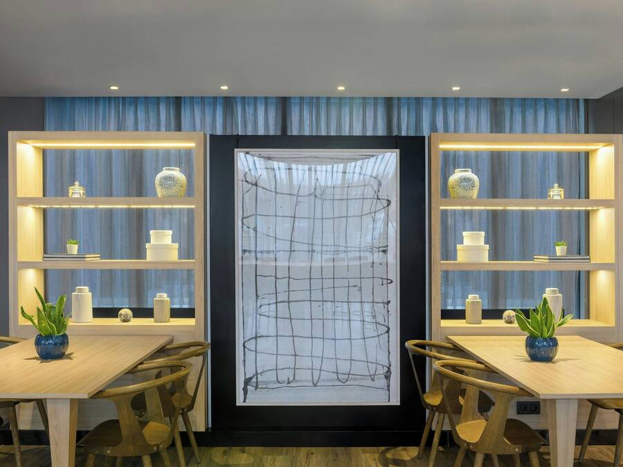 Un comedor moderno con mesas y sillas de madera, dos estantes iluminados con objetos decorativos, y una gran obra de arte abstracta en la pared.