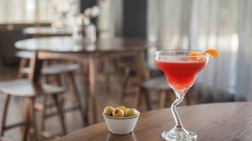 Una copa de martini con una bebida roja y una cáscara de naranja sobre una mesa de madera.