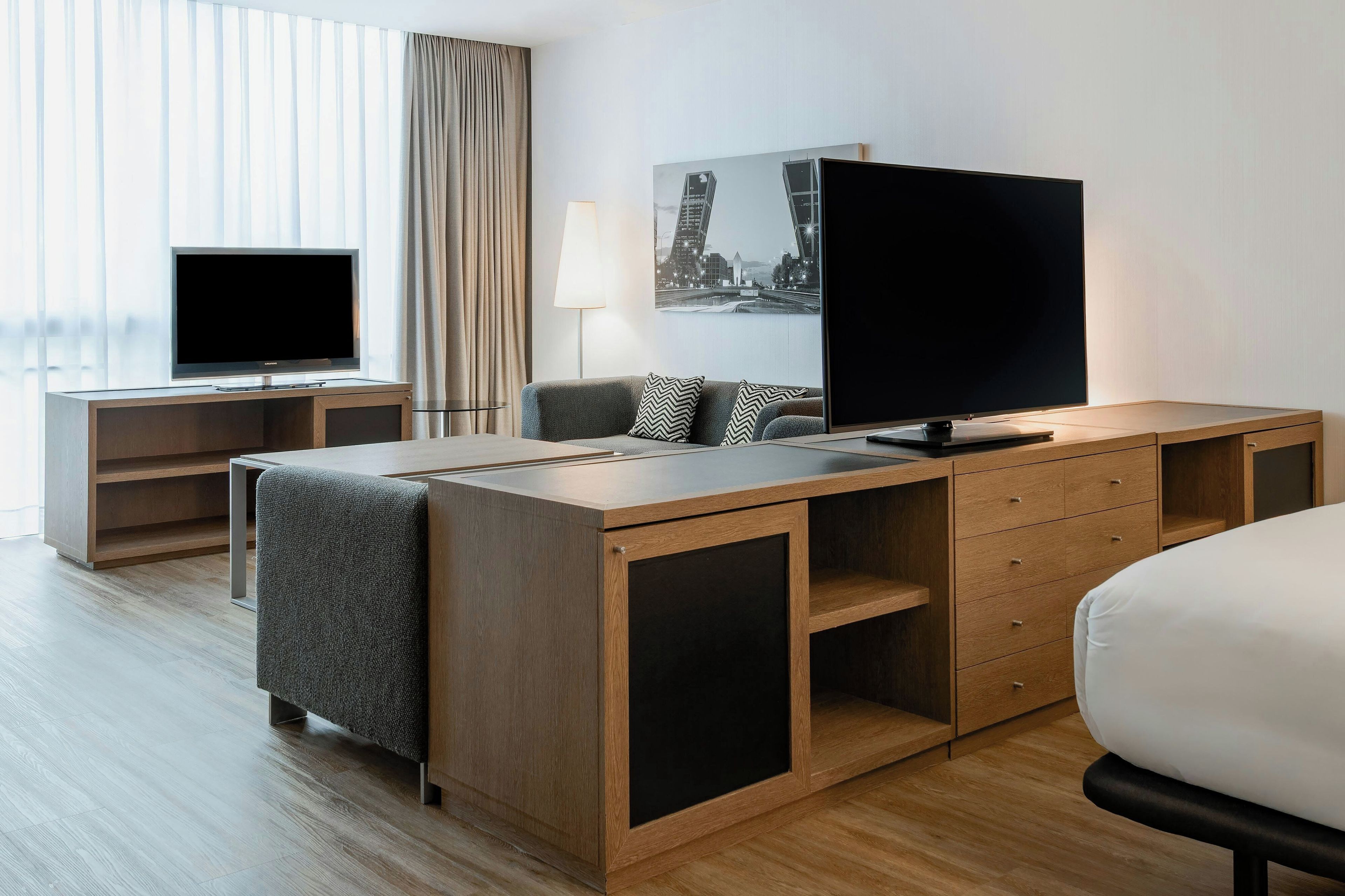 A hotel room with a desk, a television, a lamp, and a bed.