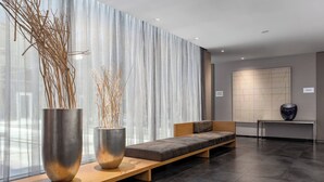 A modern waiting area with a sofa, two large metallic vases with branches, and a bench. - AC Hotel La Finca by Marriott (Pozuelo de Alarcon)