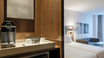 Habitación de hotel con pared de paneles de madera, una cafetera, una bandeja con tazas, una cama, un sofá y una lámpara.