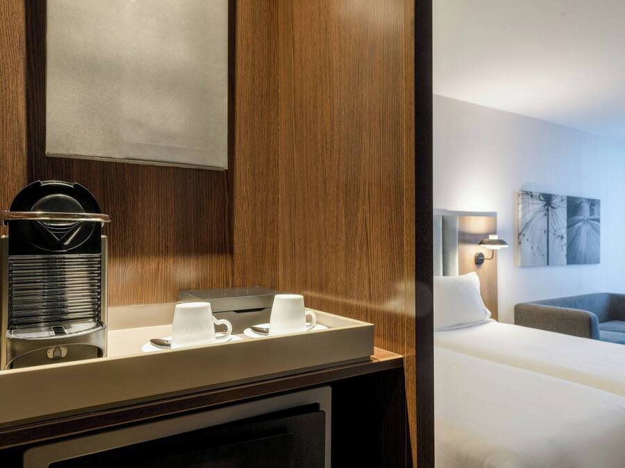 Habitación de hotel con pared de paneles de madera, una cafetera, una bandeja con tazas, una cama, un sofá y una lámpara.