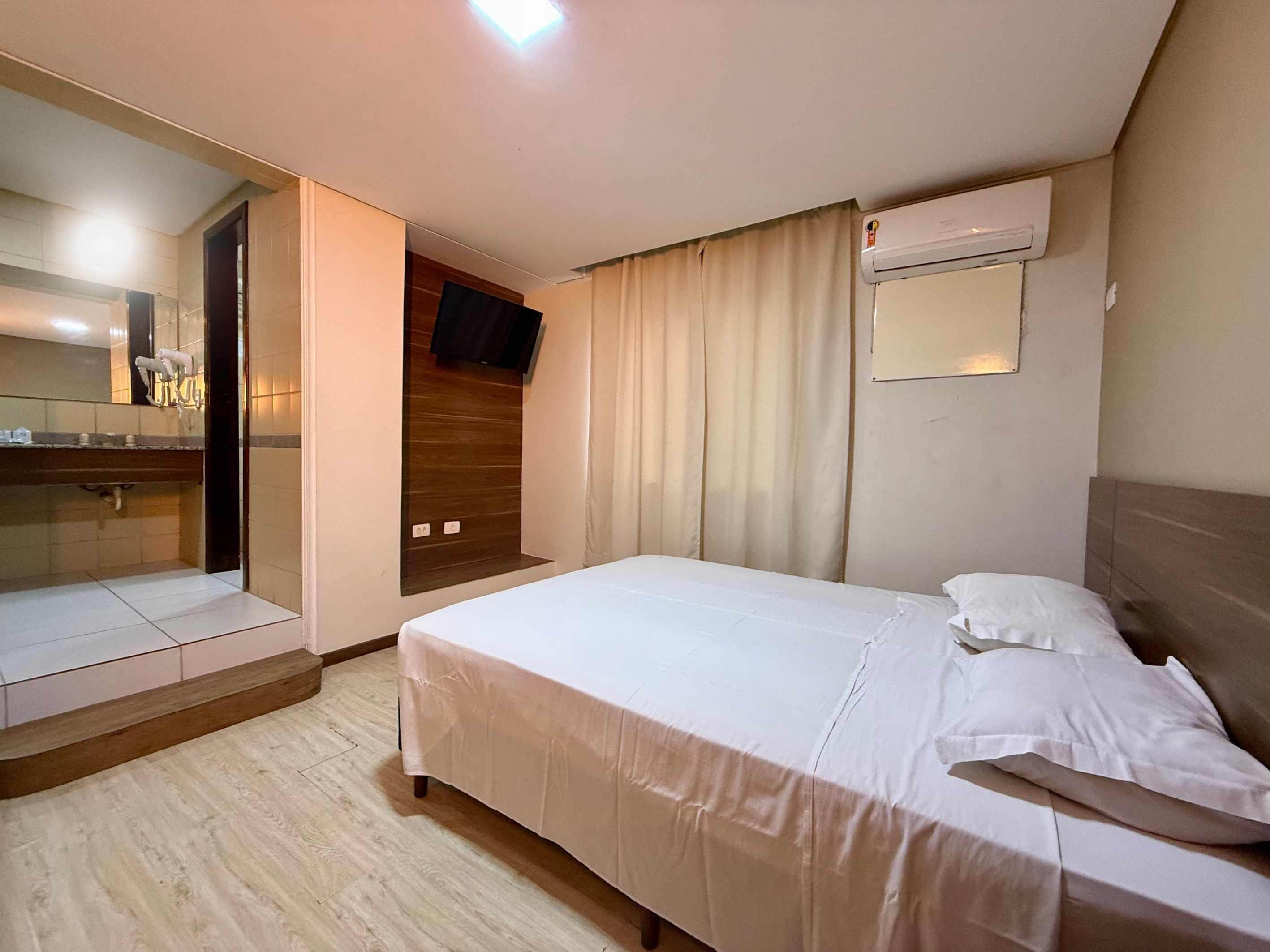 Quarto de hotel com cama, espelho, televisão e ar condicionado.