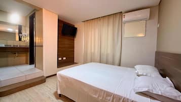 Quarto de hotel com cama, espelho, televisão e ar condicionado.