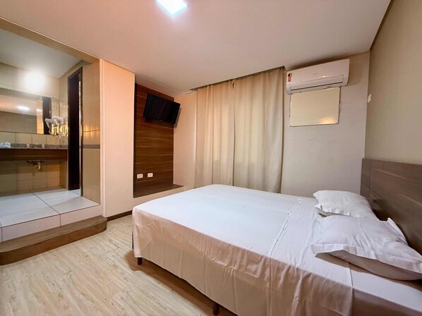 A hotel room with a bed, a mirror, a TV, and an air conditioning unit. - Granville Hotel (Curitiba)