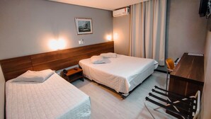 A hotel room with two beds, a desk, a chair, a TV, and an air conditioning unit. - Granville Hotel (Curitiba)
