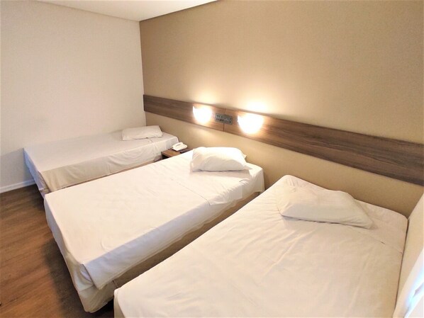 Habitación de hotel con dos camas individuales, cabecero de madera y una lámpara fijada a la pared.